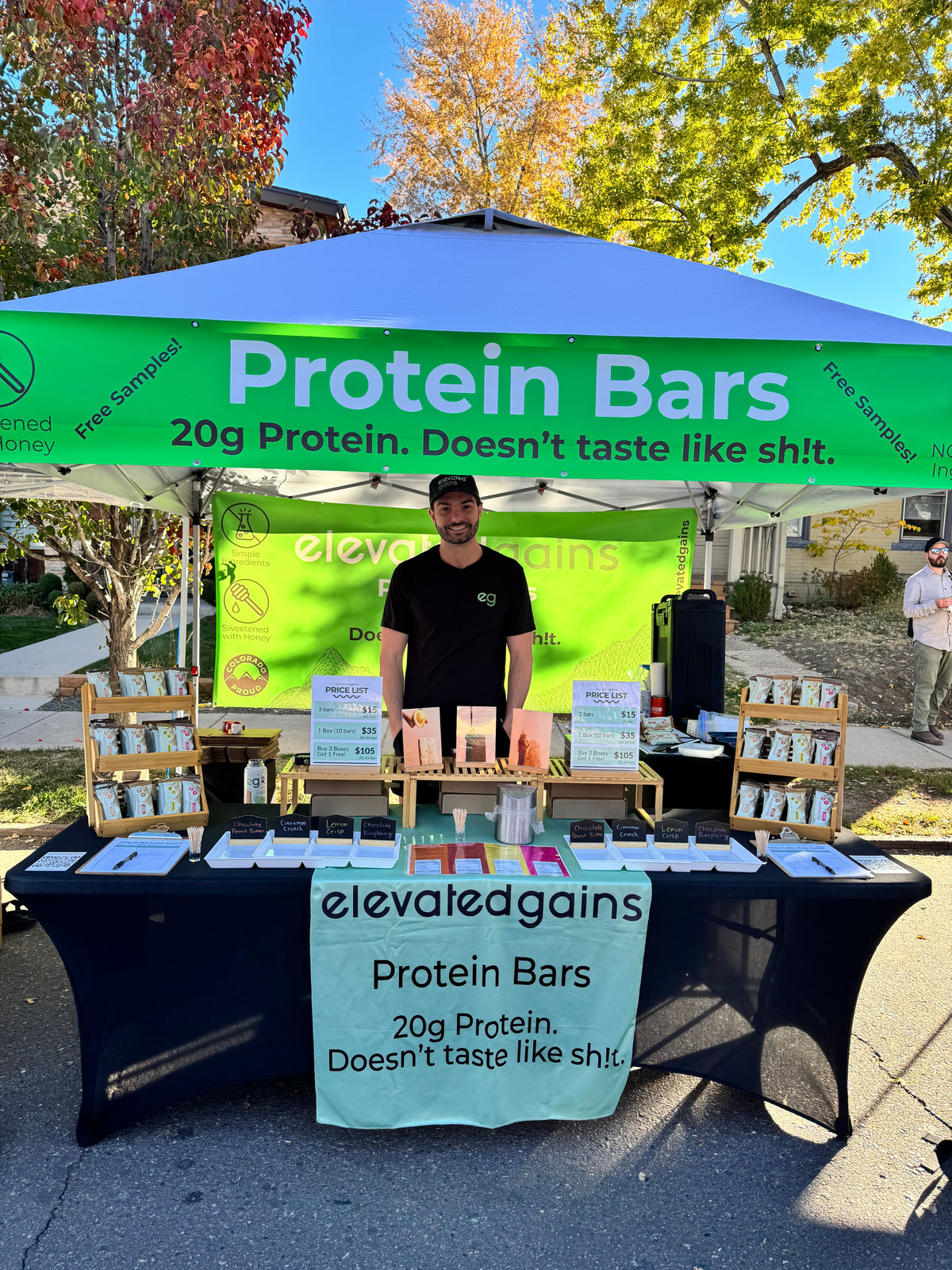 Scott at the Elevated Gains farmers market tent under our sign: 20g Protein. Doesn’t taste like shit.